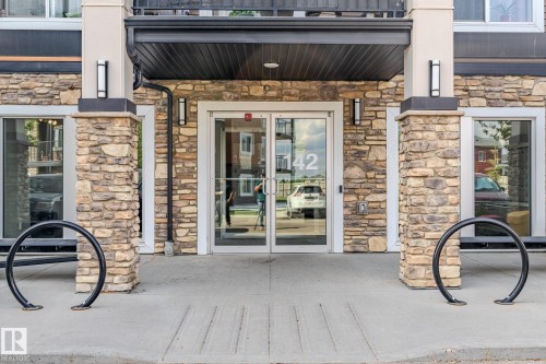 Building entrance featuring a stone facade, glass doors, and integrated lighting fixtures - 107 142 Ebbers Boulevard, Edmonton, AB 