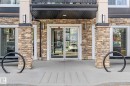 Building entrance featuring a stone facade, glass doors, and integrated lighting fixtures - 107 142 Ebbers Boulevard, Edmonton, AB 