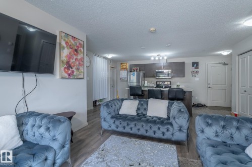 Open-concept living space featuring wood-finish flooring, a kitchen with dark cabinetry, stainless steel appliances, and a breakfast bar with seating - 107 142 Ebbers Boulevard, Edmonton, AB 