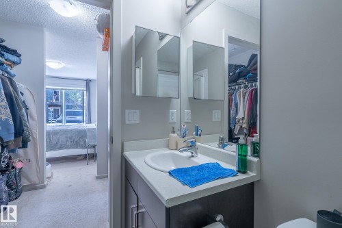 Bathroom vanity with a single basin sink, a light-toned countertop, and dark wood-finish cabinetry - 107 142 Ebbers Boulevard, Edmonton, AB 