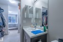 Bathroom vanity with a single basin sink, a light-toned countertop, and dark wood-finish cabinetry - 107 142 Ebbers Boulevard, Edmonton, AB 