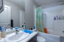 Bathroom featuring an integrated sink, chrome faucet, wall-mounted mirror, white bathtub with a tile surround, and a white toilet - 107 142 Ebbers Boulevard, Edmonton, AB 