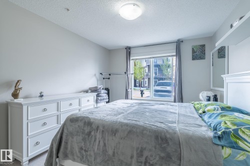 Carpeted bedroom featuring a large window, a ceiling-mounted light fixture, and light-toned walls - 107 142 Ebbers Boulevard, Edmonton, AB 