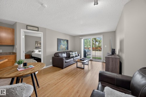 Open-concept living area featuring wood-finish flooring, a sliding glass door to an outdoor balcony, an entryway to an additional room, a ceiling-mounted light fixture, and light-toned wall paint - 111 3425 19, Edmonton, AB 