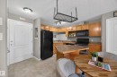 Open-concept kitchen featuring light wood cabinetry, black appliances, a central island with countertop seating, tiled flooring, and a ceiling-mounted pot rack - 111 3425 19, Edmonton, AB 