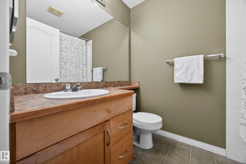 Bathroom featuring a light wood-finish vanity with an integrated basin, a stone-look countertop, an expansive wall mirror, and neutral wall paint - 111 3425 19, Edmonton, AB 
