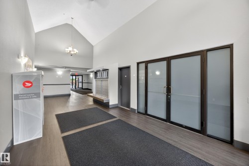 Spacious common area featuring vaulted ceilings with a chandelier, wood-finish flooring, and frosted glass entryway doors - 111 3425 19, Edmonton, AB 
