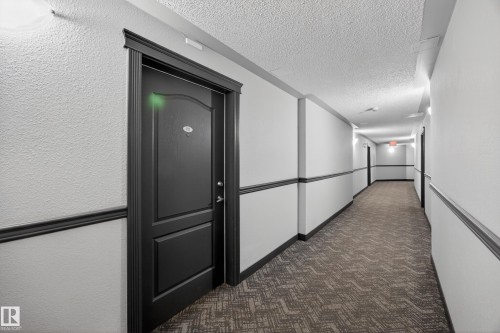 Building corridor featuring a textured ceiling, neutral-toned walls, dark trim, and patterned carpeting - 111 3425 19, Edmonton, AB 
