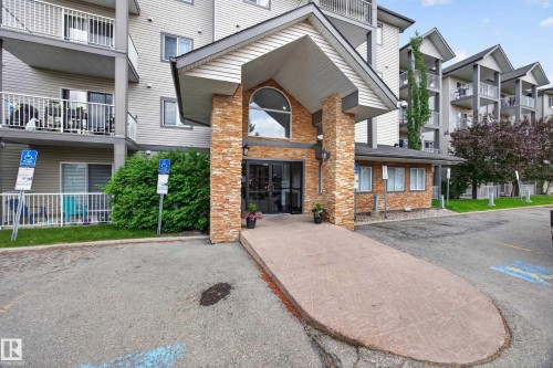 Apartment building exterior featuring a stone-clad entrance with an arched window above double glass doors - 111 3425 19, Edmonton, AB 