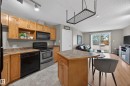 Open-concept living space featuring a kitchen with wood cabinetry, black and stainless steel appliances, and a peninsula with seating - 111 3425 19, Edmonton, AB 