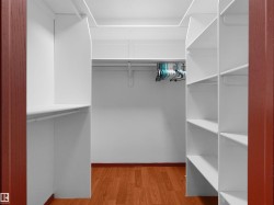 Walk-in closet featuring white shelving units, hanging rods, and wood-finish flooring - 