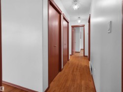 Hallway featuring wood-finish flooring, white walls, and wood trim - 