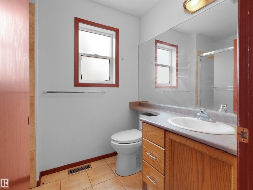 Bathroom featuring a single-pane window with wood-finish trim, a wood-finish vanity with an integrated sink, a large wall-mounted mirror, and tile flooring - 2832 36B Avenue, Edmonton, AB - Indoor Photo Showing Bathroom