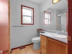 Bathroom featuring a single-pane window with wood-finish trim, a wood-finish vanity with an integrated sink, a large wall-mounted mirror, and tile flooring - 