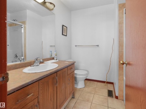 Bathroom featuring a vanity with wood-finish cabinetry, a single basin sink, a large wall-mounted mirror, and a ceramic tile floor - 2832 36B Avenue, Edmonton, AB - Indoor Photo Showing Bathroom