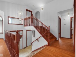 Two-story entry featuring hardwood flooring, natural wood staircase with balusters, a clear glass chandelier, and a transom window - 
