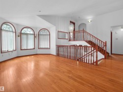 Spacious interior featuring wood-finish flooring, a grand staircase with wooden railings, and multiple arched windows with vertical blinds - 