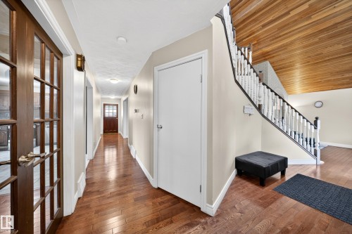 Hallway featuring wood-finish flooring, a white-painted staircase with black handrails, and a wood-paneled ceiling - 34 Grand Meadow Crescent, Edmonton, AB 