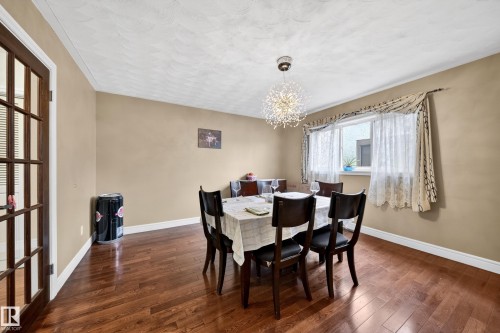 Dining area featuring wood-finish flooring, a contemporary chandelier, and a large window - 34 Grand Meadow Crescent, Edmonton, AB 
