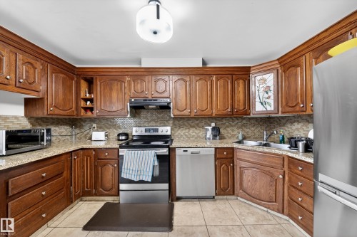 U-shaped kitchen featuring wood cabinetry, light-toned granite countertops, and a mosaic tile backsplash - 34 Grand Meadow Crescent, Edmonton, AB 