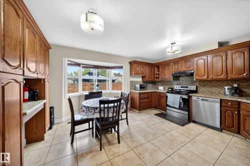 Kitchen featuring extensive wood cabinetry, light-toned tile flooring, a bay window, stainless steel appliances, and built-in overhead lighting fixtures - 34 Grand Meadow Crescent, Edmonton, AB 