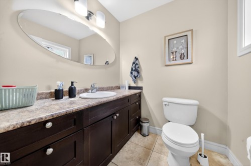 Bathroom featuring an oval mirror, a vanity with dark wood-finish cabinetry, a white ceramic sink, a laminate countertop, and tile flooring - 34 Grand Meadow Crescent, Edmonton, AB 