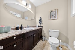 Bathroom featuring an oval mirror, a vanity with dark wood-finish cabinetry, a white ceramic sink, a laminate countertop, and tile flooring - 
