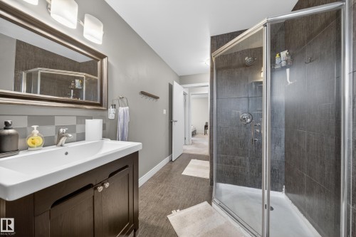 Full bathroom featuring a dark wood-finish vanity with a white countertop and basin sink, a framed mirror, and a glass-enclosed shower with dark tile surround - 34 Grand Meadow Crescent, Edmonton, AB 