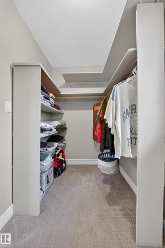 Walk-in closet featuring light gray wall paint, white baseboards, light gray patterned carpeting, and white built-in shelving units - 34 Grand Meadow Crescent, Edmonton, AB 