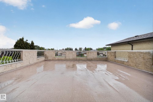 Expansive rooftop patio featuring a light-toned textured surface, decorative white metal railings, and a stucco-textured perimeter wall - 34 Grand Meadow Crescent, Edmonton, AB 