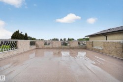 Expansive rooftop patio featuring a light-toned textured surface, decorative white metal railings, and a stucco-textured perimeter wall - 