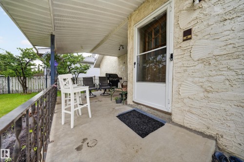 Concrete covered patio featuring a screen door entry, decorative textured exterior wall, and a wrought iron railing - 34 Grand Meadow Crescent, Edmonton, AB 