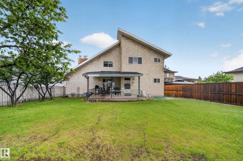 Expansive rear yard featuring a covered patio, a full privacy fence, mature trees along the property line, and a stucco exterior - 34 Grand Meadow Crescent, Edmonton, AB 