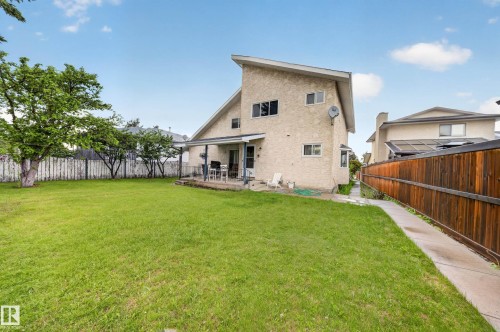 Expansive backyard featuring a large green lawn, mature trees, a concrete patio, and a covered porch - 34 Grand Meadow Crescent, Edmonton, AB 