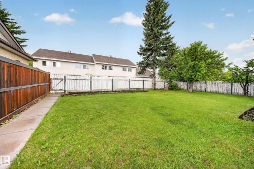 Expansive backyard featuring a lush green lawn, mature trees, a privacy wood fence, and a concrete pathway - 34 Grand Meadow Crescent, Edmonton, AB 