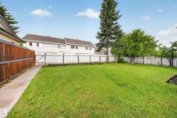 Expansive backyard featuring a lush green lawn, mature trees, a privacy wood fence, and a concrete pathway - 