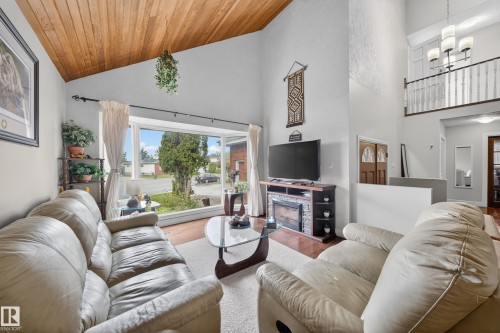 Expansive living area featuring a vaulted wood-paneled ceiling, large picture window, and a stone-clad electric fireplace - 34 Grand Meadow Crescent, Edmonton, AB 