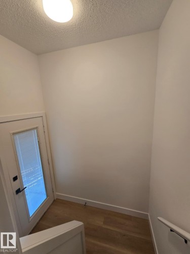 Stairwell entry featuring wood-finish flooring, white baseboards, a white door with a frosted glass panel, and a flush-mount ceiling light fixture - 18526 86A Avenue, Edmonton, AB - Indoor Photo Showing Other Room