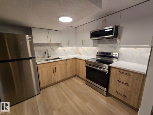 Contemporary kitchen featuring stainless steel appliances, light wood-finish lower cabinetry, white upper cabinetry, and white countertops with a matching backsplash - 18526 86A Avenue, Edmonton, AB - Indoor Photo Showing Kitchen With Stainless Steel Kitchen With Double Sink