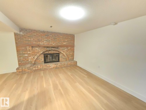 Spacious room featuring a brick fireplace with an arched firebox, light wood-finish flooring, white walls, and recessed lighting - 18526 86A Avenue, Edmonton, AB - Indoor Photo Showing Living Room With Fireplace
