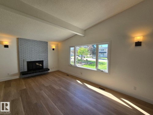 Spacious living area featuring a vaulted ceiling with exposed beams, light wood-finish flooring, and a painted brick fireplace with a black hearth - 18526 86A Avenue, Edmonton, AB - Indoor Photo Showing Living Room With Fireplace