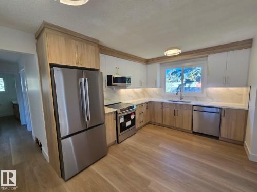 Renovated kitchen featuring wood-finish flooring, two-tone cabinetry, stainless steel appliances, and under-cabinet lighting - 18526 86A Avenue, Edmonton, AB - Indoor Photo Showing Kitchen With Stainless Steel Kitchen