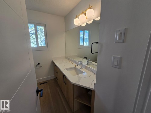 Bathroom vanity featuring a quartz countertop with integrated sink, wood-finish cabinetry with matte black hardware, and a large wall-mounted mirror - 18526 86A Avenue, Edmonton, AB - Indoor Photo Showing Bathroom