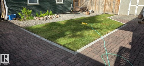 Expansive brick paver patio surrounding a central lawn area, featuring a decorative rock garden with plantings, and a wooden privacy fence - 6704 93 Street, Edmonton, AB 
