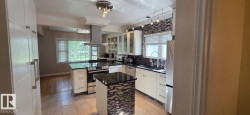 Modern kitchen featuring white cabinetry, black countertops, a mosaic tile backsplash, and stainless steel appliances - 