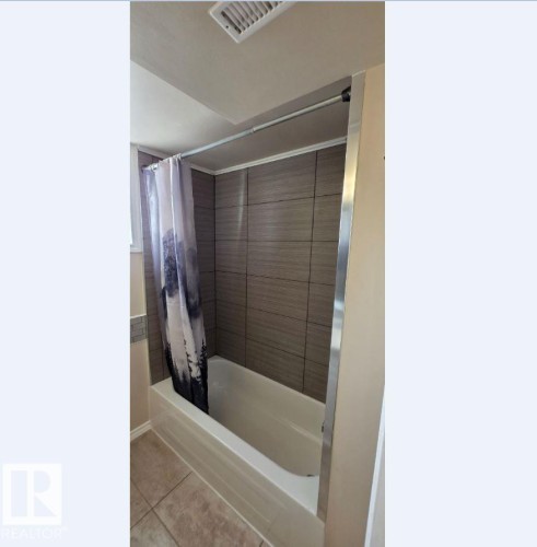 Bathtub with neutral-toned horizontal tile surround and complementary accent tile border - 6704 93 Street, Edmonton, AB 