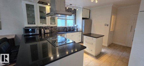 Kitchen featuring a built-in cooktop, stainless steel range hood, dark countertops, white cabinetry, and tile flooring - 6704 93 Street, Edmonton, AB 