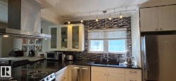Modern kitchen with black countertops, a mosaic tile backsplash, and white cabinetry - 