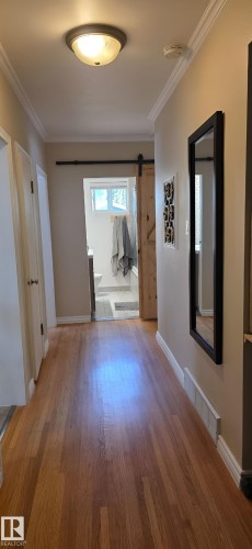 Hardwood flooring hallway leading to a bathroom with a sliding barn door - 6704 93 Street, Edmonton, AB 