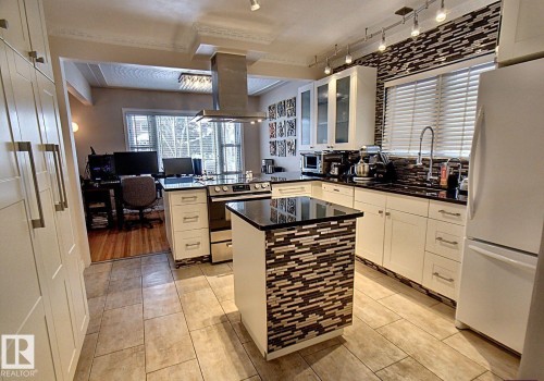 Kitchen featuring tile flooring, white cabinetry with contemporary hardware, black countertops, and a full-height mosaic tile backsplash - 6704 93 Street, Edmonton, AB 